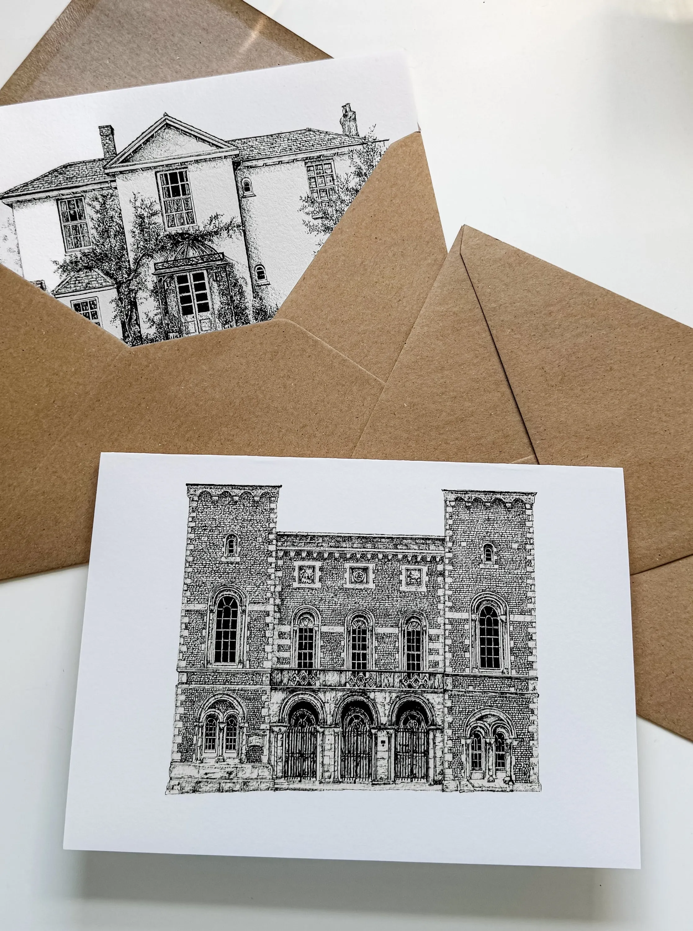 Two black ink greeting cards showing The Pig in the South Downs and Arundel Town Hall, laid on brown kraft envelopes