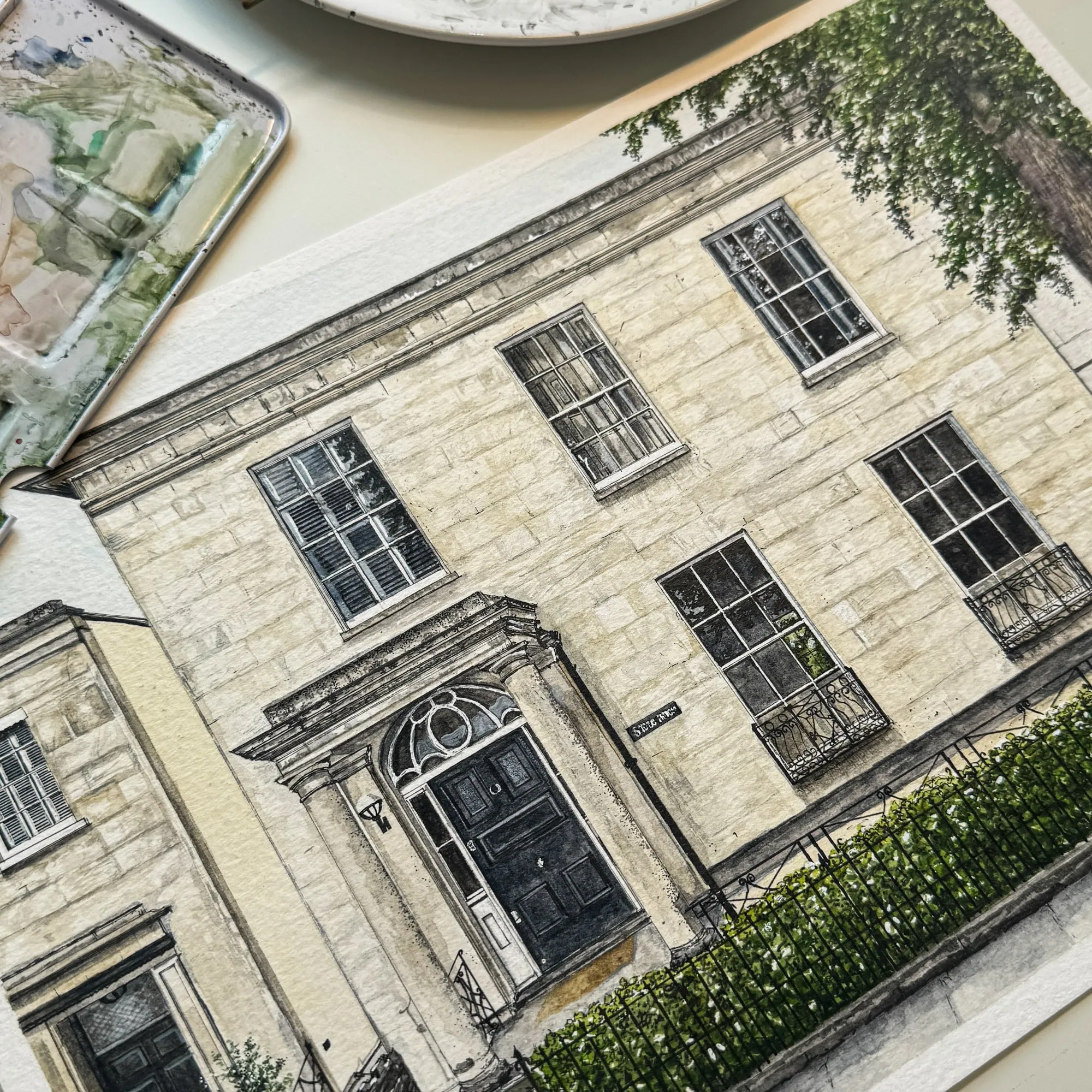 Detailed ink and watercolour drawing of a cream Bath stone townhouse, photographed on a desk beside paints and brushes